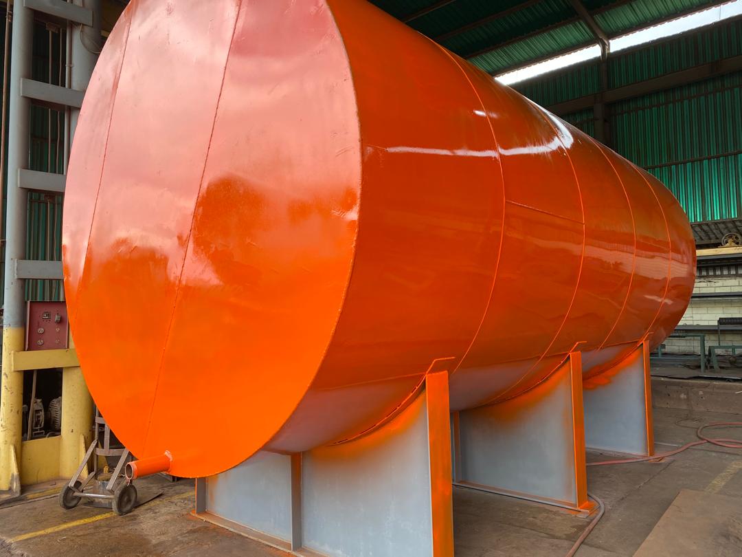Tanque metálico cilíndrico naranja sostenido por bases en un taller